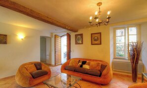 Ein Wohnzimmer mit Sofa, Sessel, Glastisch, einer Kronleuchter, gerahmten Bildern und einem Fenster mit Blick.
