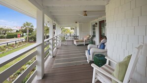 Eine überdachte Veranda mit weißen Geländern, einem Holzboden und Blick auf einen Garten sowie Gebäude in der Ferne.