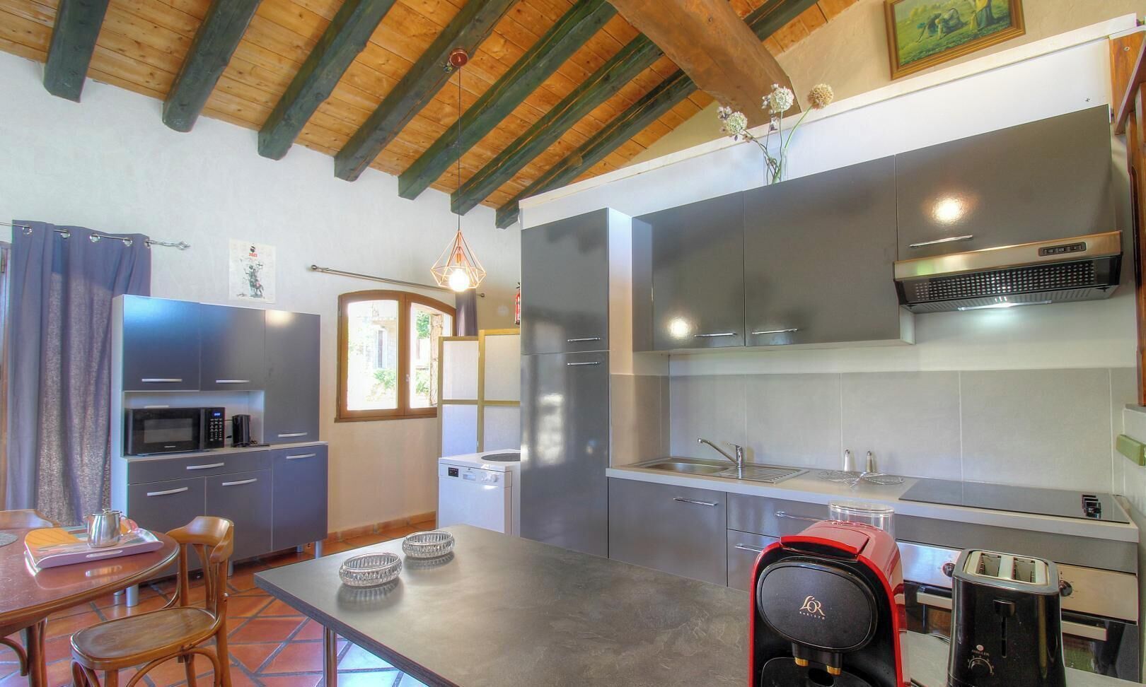 Eine kleine Küche mit modernen Geräten, ein Essbereich mit Tisch und Stühlen sowie eine Holzbalkendecke.