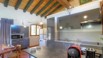 Eine kleine Küche mit modernen Geräten, ein Essbereich mit Tisch und Stühlen sowie eine Holzbalkendecke.