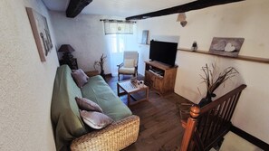 Una sala de estar con un sofá verde, una mesa de centro de madera, un televisor sobre un mueble de madera, una silla y una escalera.