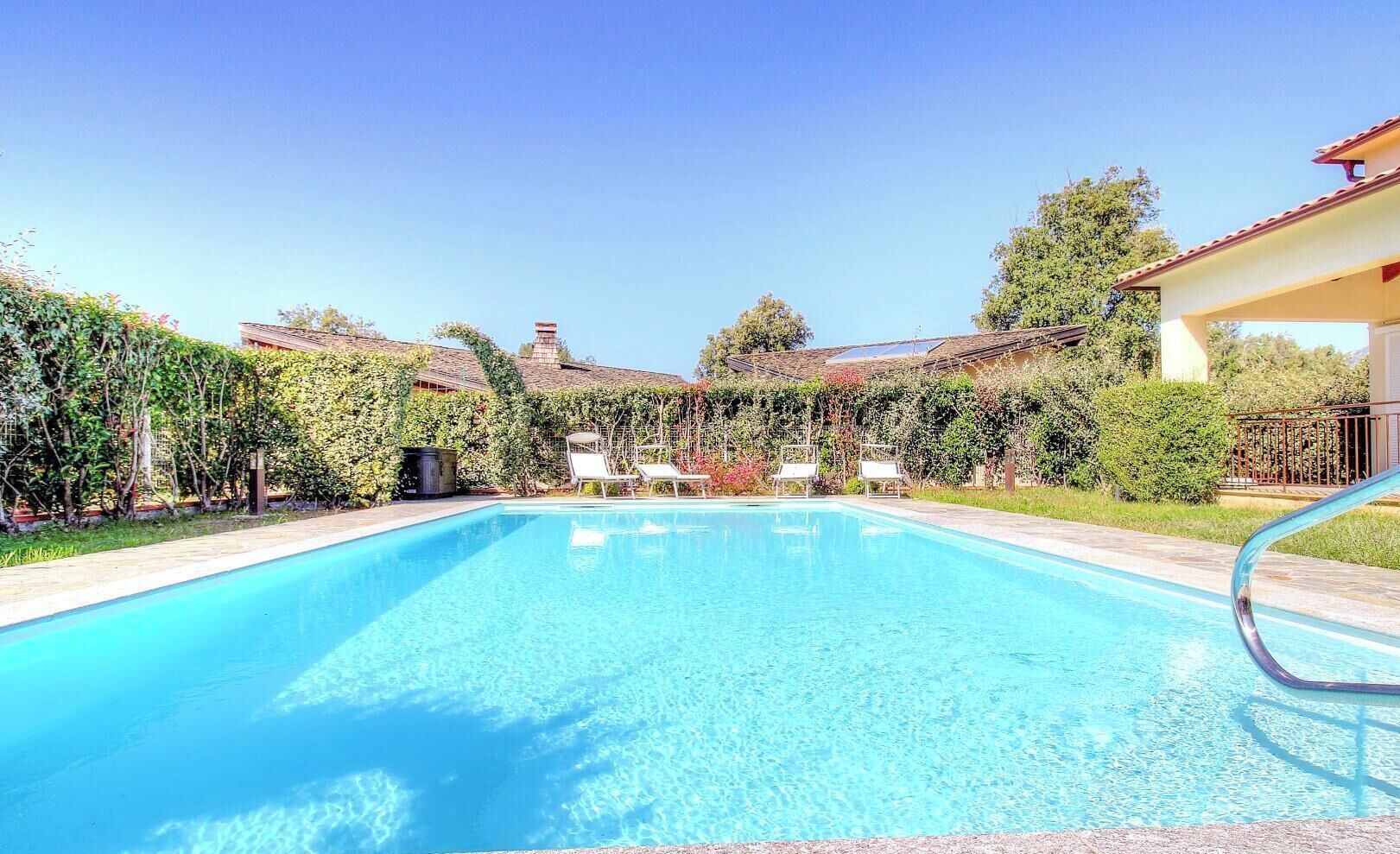 Una piscina cristalina con sillones de descanso, rodeada de vegetación y edificios.