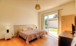 Ein Schlafzimmer mit Bett, Nachttischlampen, einem Schreibtisch und einer Schiebetür zu einem Balkon.