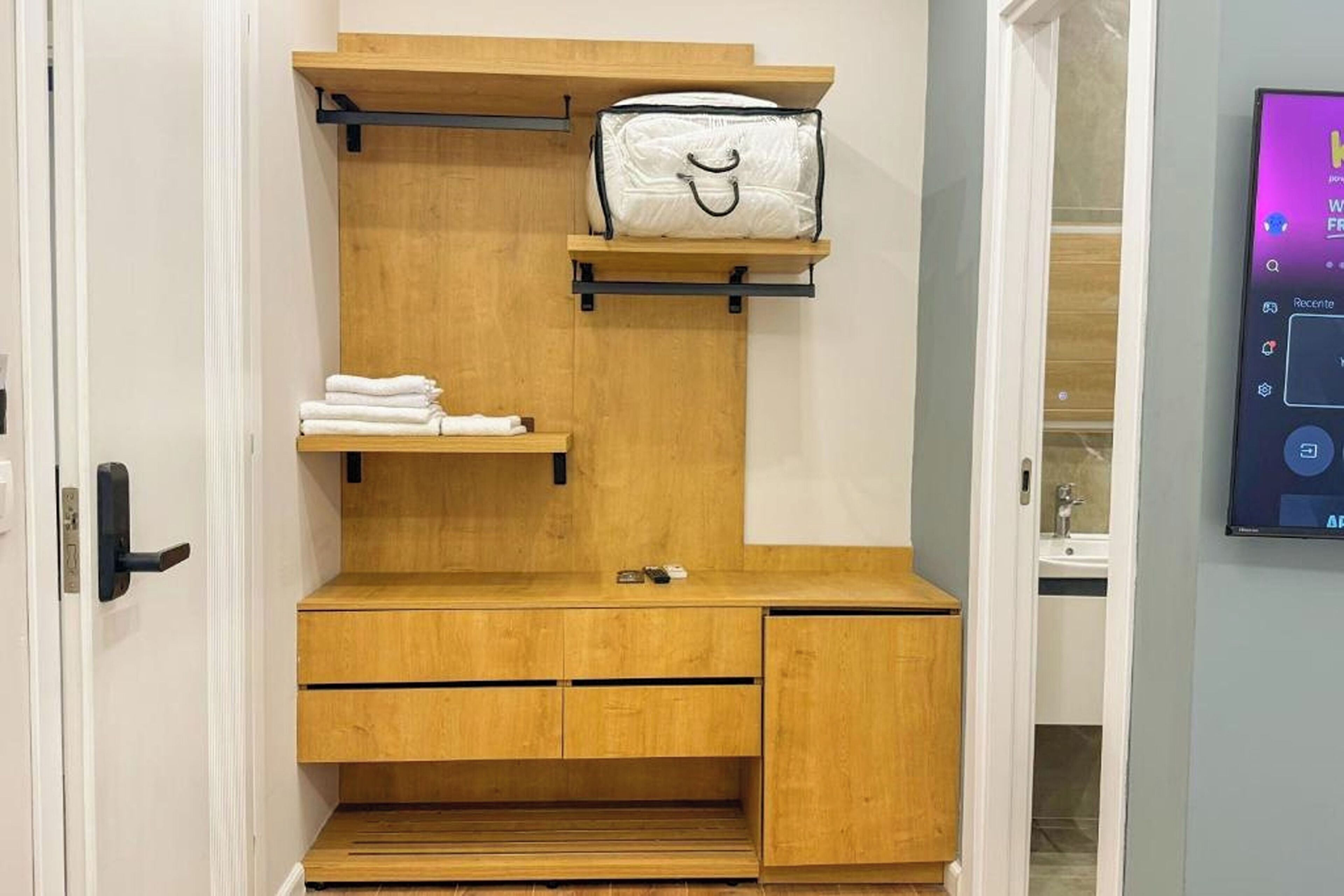 A compact room with a wooden vanity, a towel rack, and a small shelf.