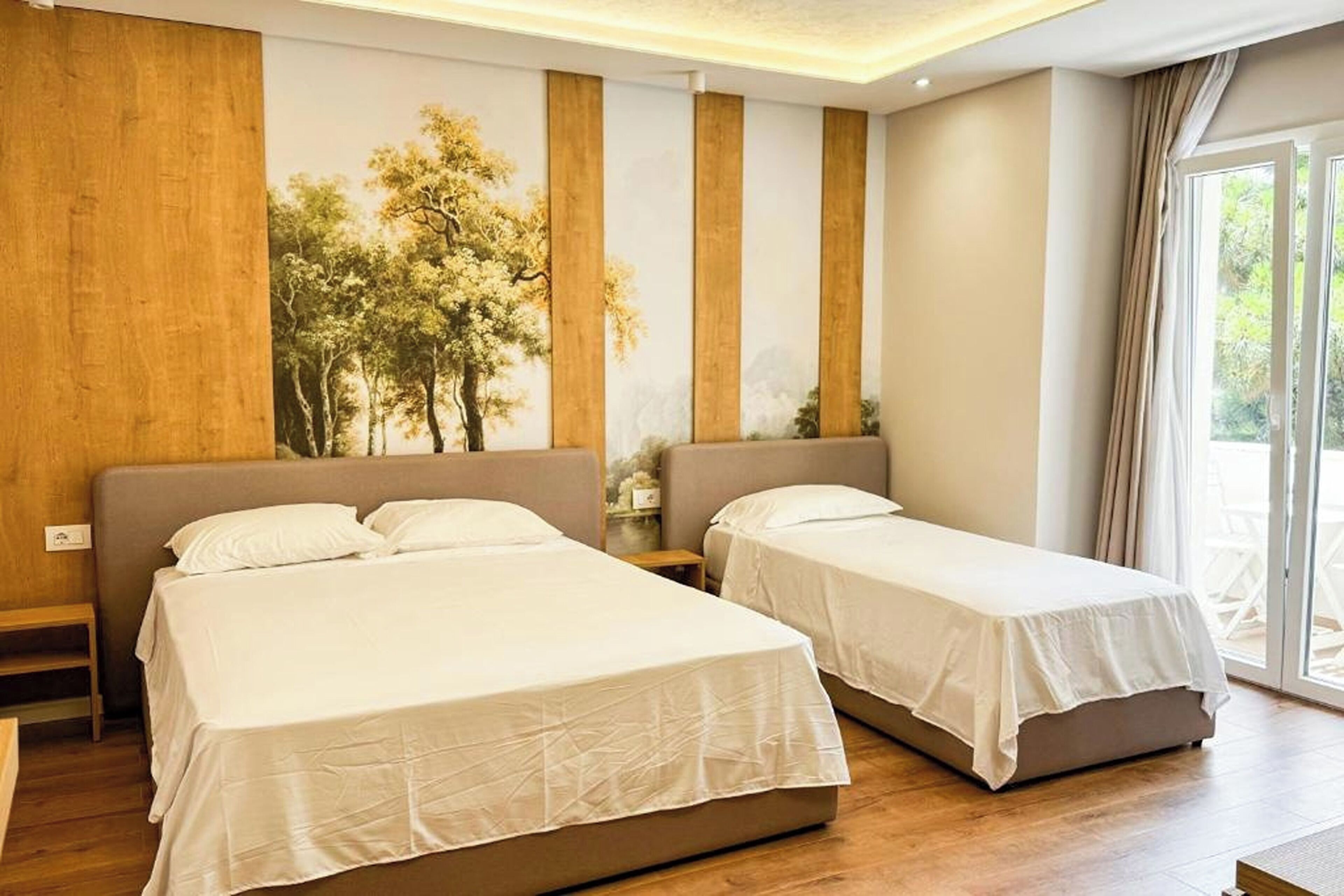 A hotel room with two beds, a large window, and a view of trees.