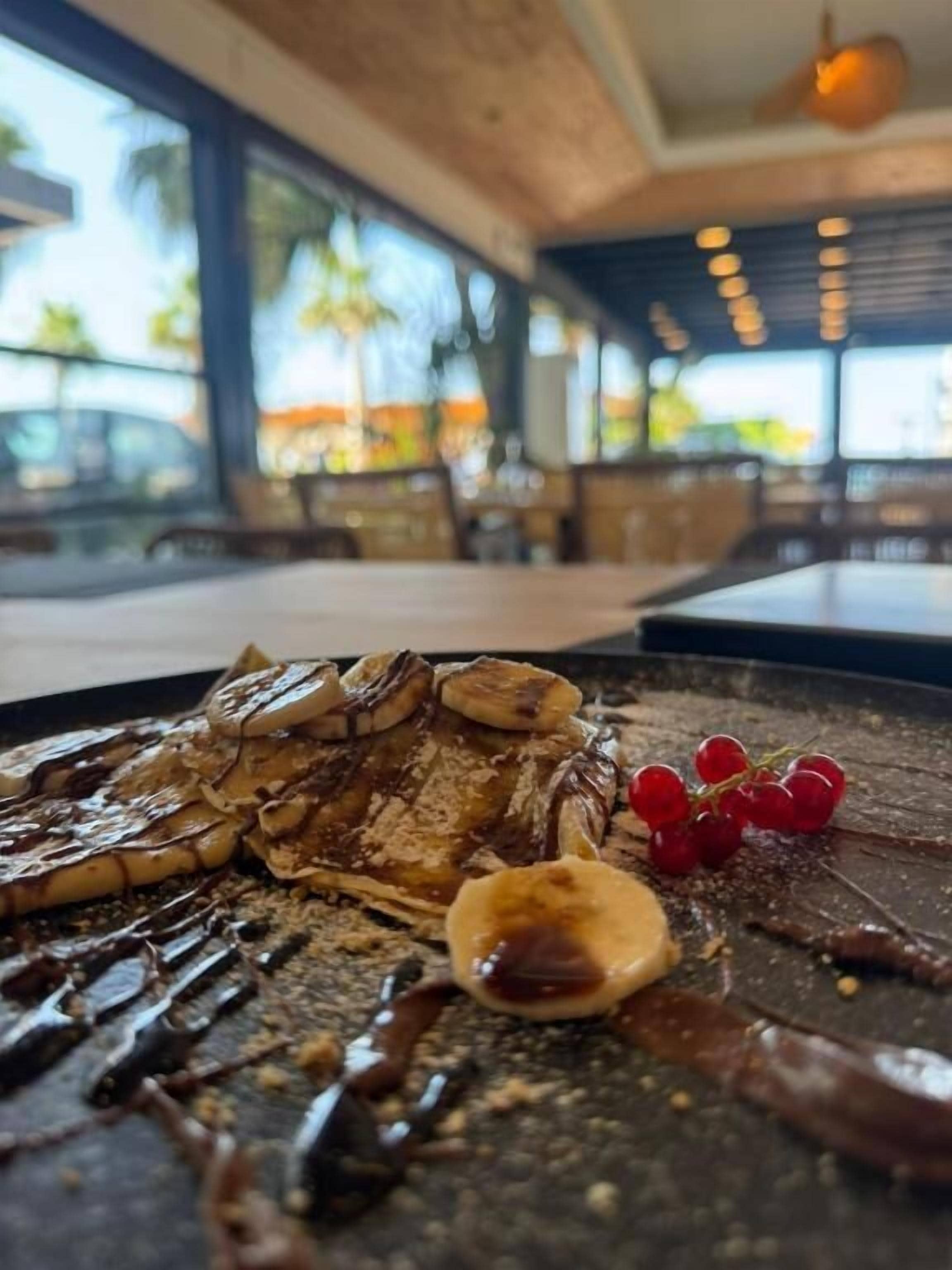Une assiette de dessert avec de la sauce au chocolat, des bananes et des raisins, posée sur une table dans un restaurant.