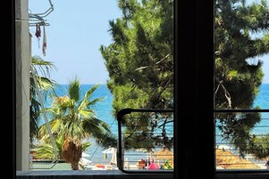 Vista a través de una ventana con baranda de metal, mostrando una playa con sombrillas y una palmera.