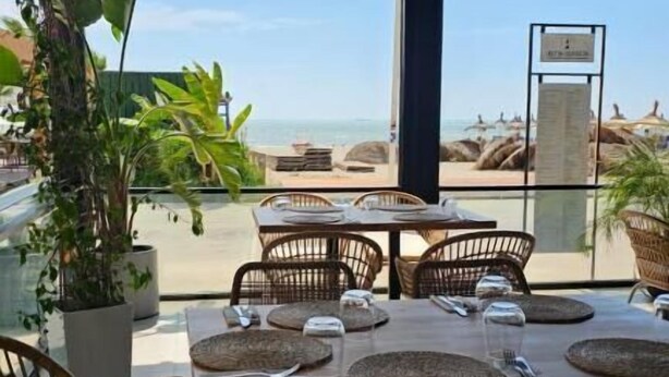 An outdoor dining area with wicker chairs and tables, overlooking a beach. - Zena Hotel (Rrashbull)