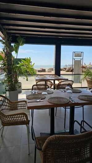 An outdoor dining area with wicker chairs and tables, overlooking a beach. - Zena Hotel (Rrashbull)