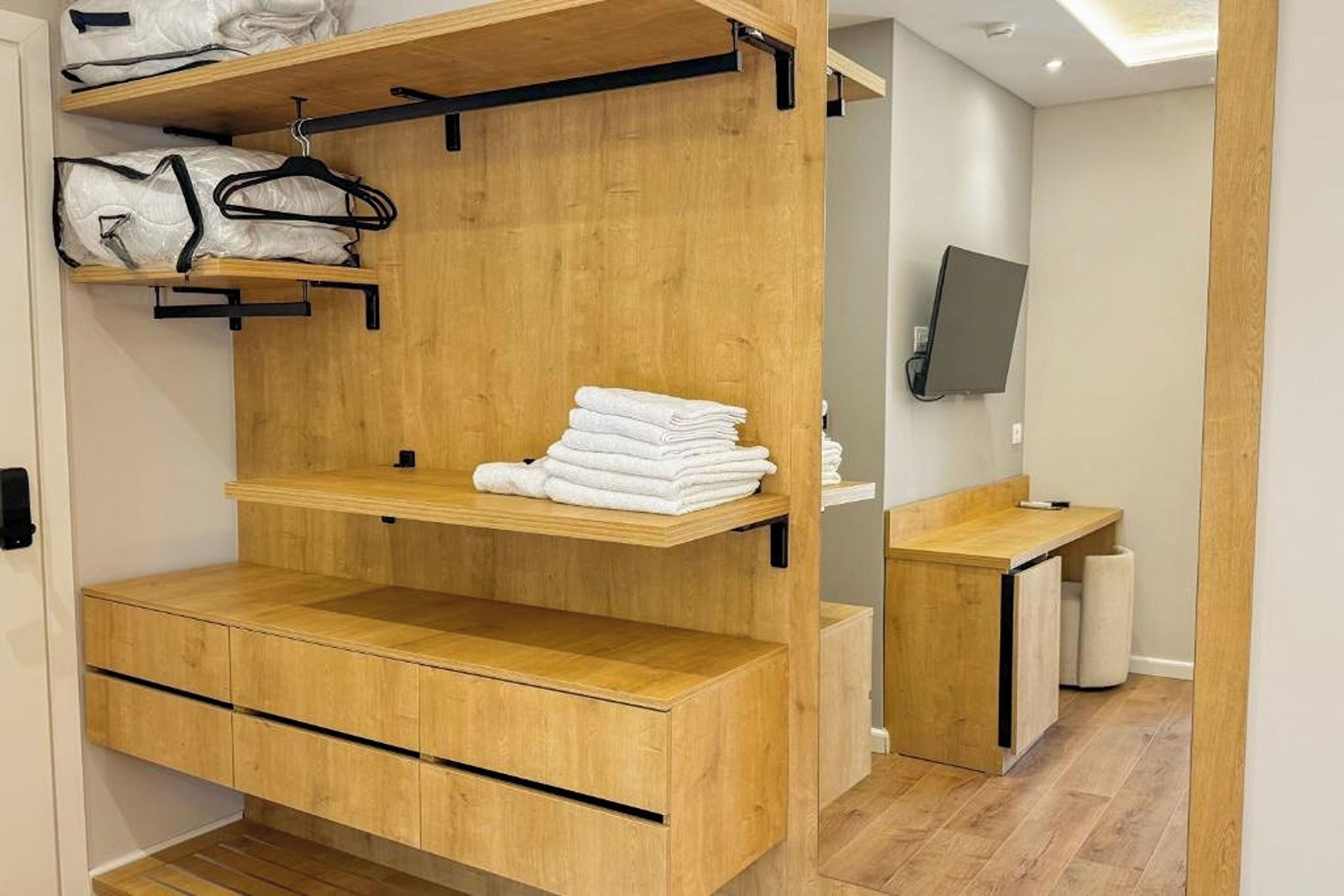 Un armario de madera con varios estantes y espacio para colgar, un escritorio pequeño de madera con espejo, y un inodoro en un baño.