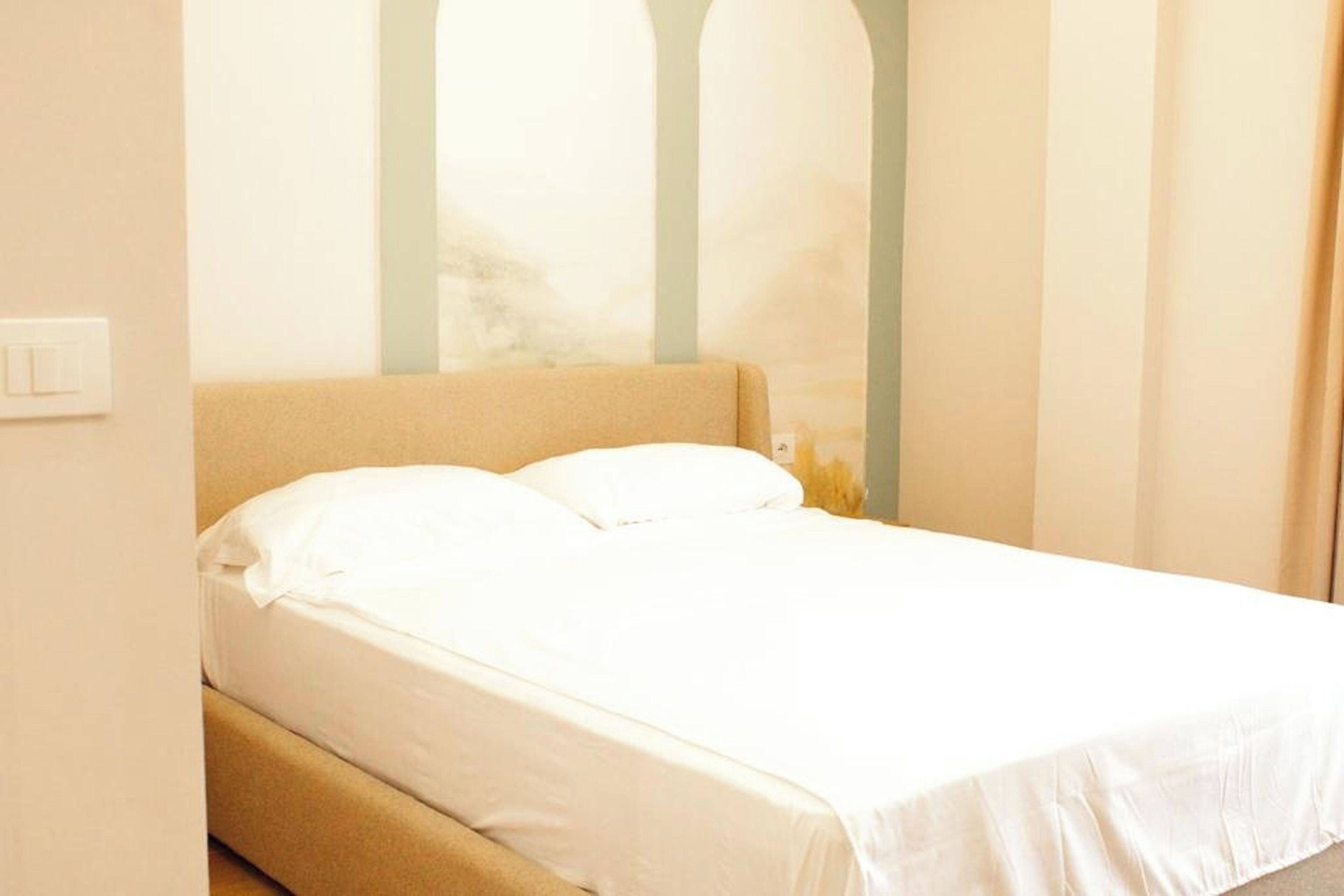 Una cama individual con ropa blanca en una habitación con pared lisa e interruptor de luz.