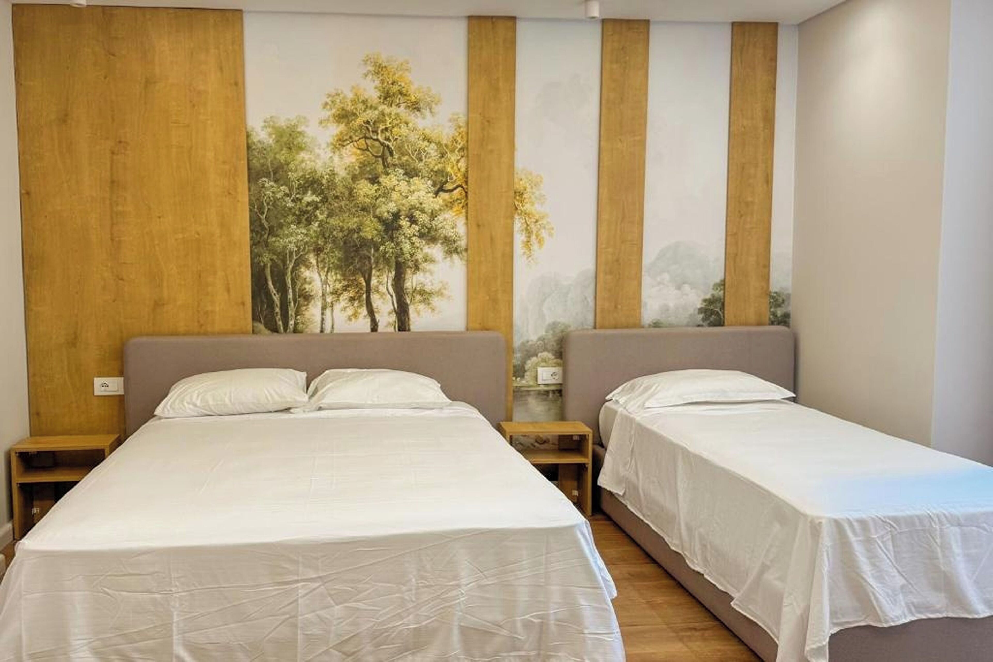 Habitació d'hotel amb dos llits, ambres de fusta i un mural gran a la paret amb representació d'arbres.