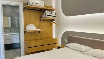 A modern bedroom with a wooden wardrobe, a bed with white linens, and a bathroom with a glass shower enclosure.