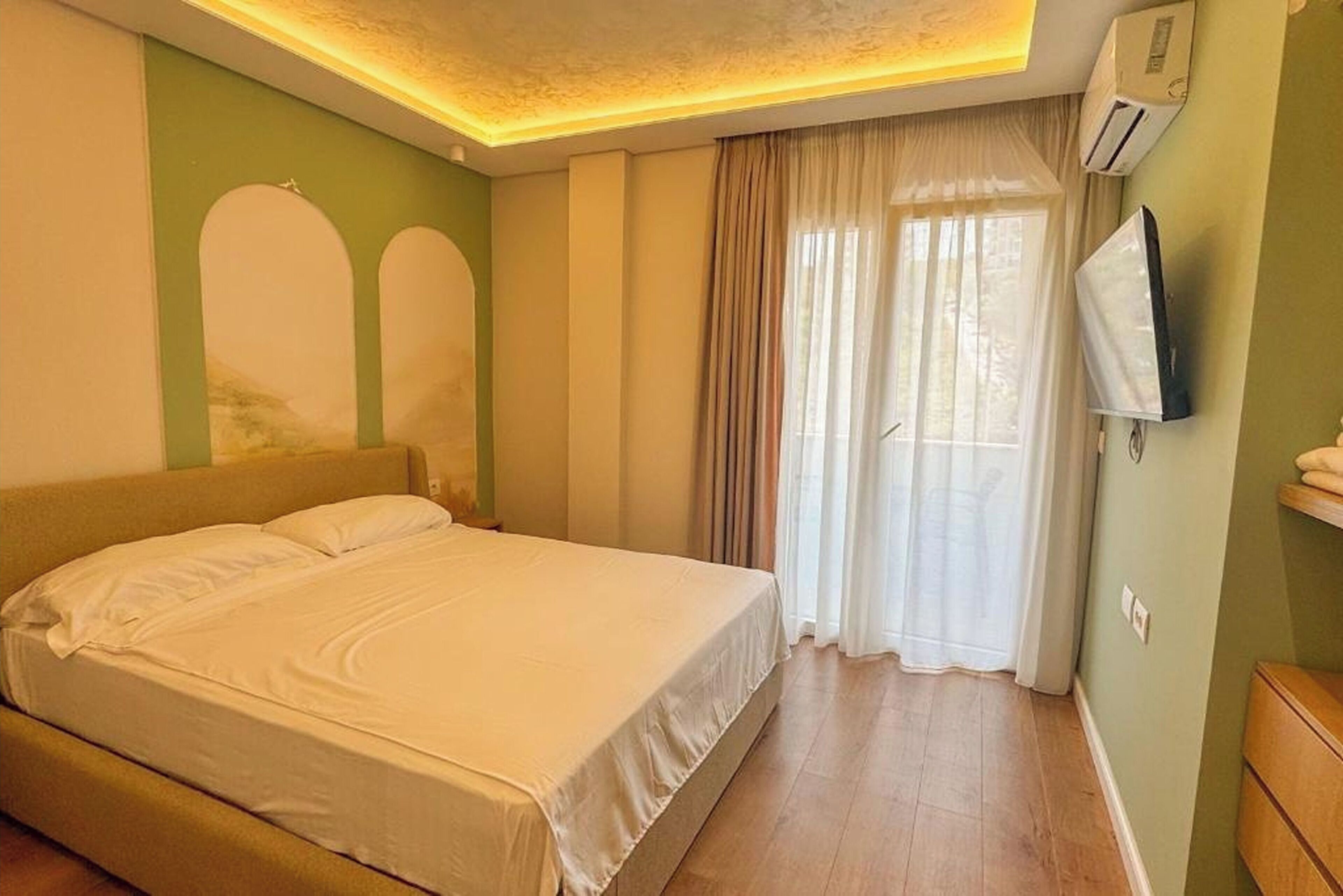 A hotel room with a bed, curtains, a television, and a wooden floor.