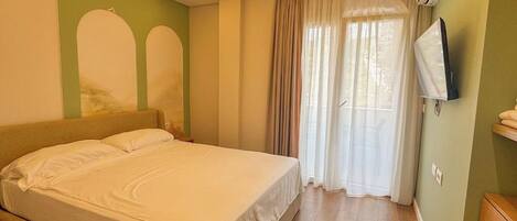 A hotel room with a bed, curtains, a television, and a wooden floor.