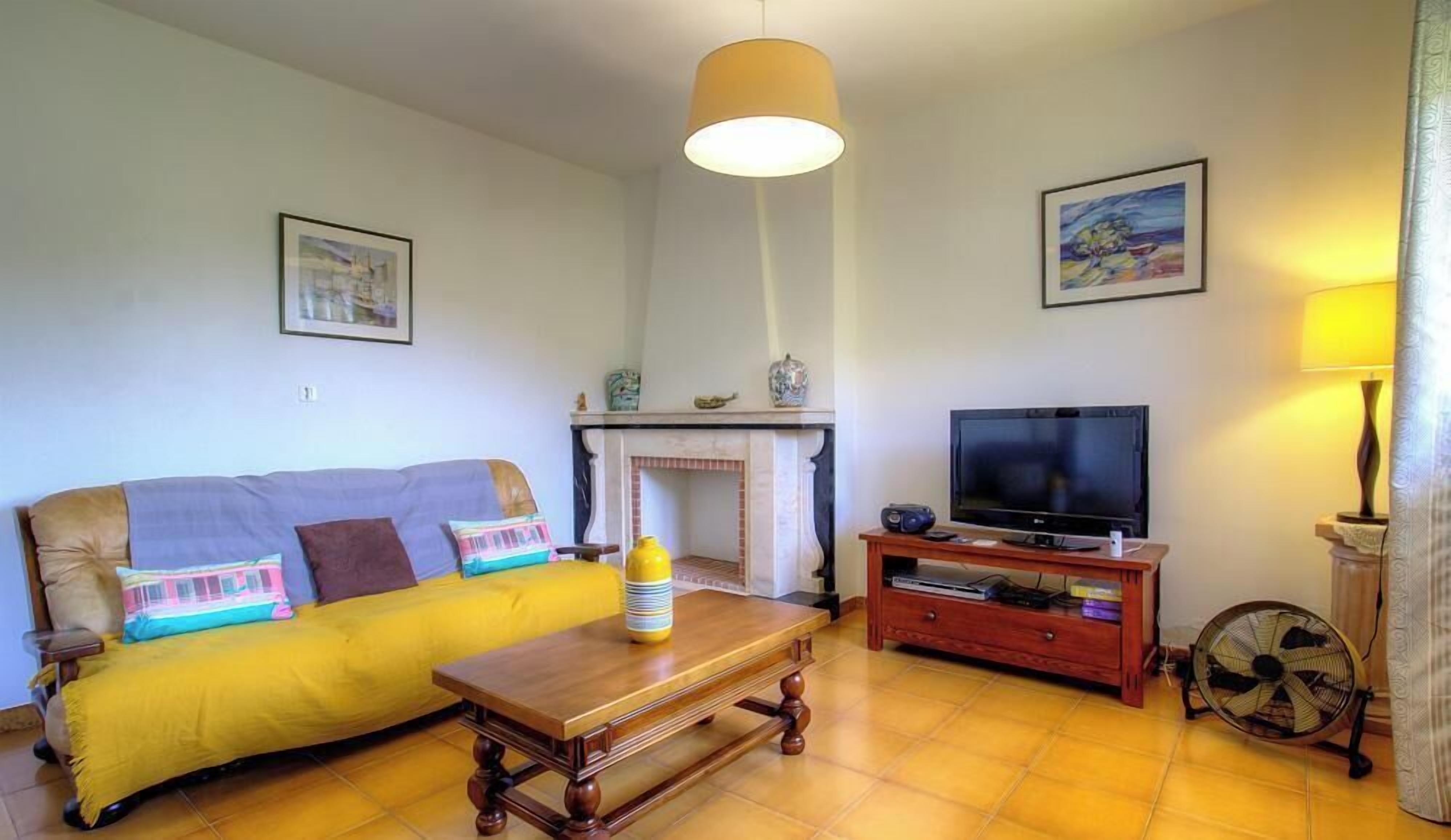 A living room with a sofa, a coffee table, a fireplace, a television, and a fan.