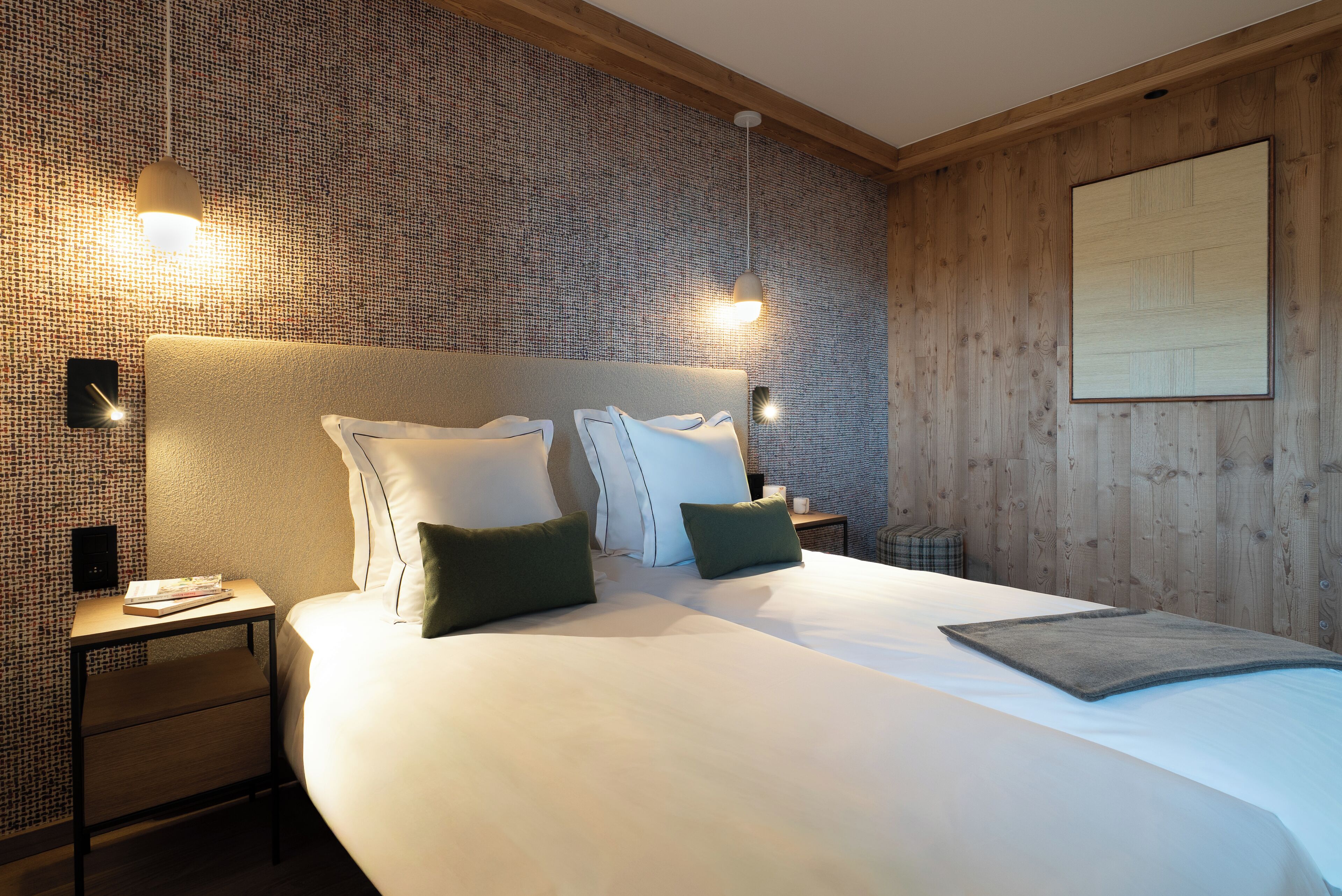 Una cama bien tendida con almohadas, una mesita de noche con un libro y una pared con un diseño texturizado.