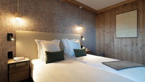 A neatly made bed with pillows, a bedside table with a book, and a wall with a textured pattern. - Résidence Barma Courchevel (Courchevel)