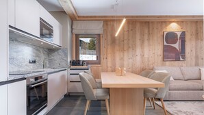 A modern kitchen with a marble countertop, wooden cabinets, and a dining area with a wooden table and chairs. - Résidence Barma Courchevel (Courchevel)