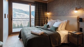 A bedroom with a large bed, a nightstand, a lamp, and a view of mountains through a balcony door. - Résidence Barma Courchevel (Courchevel)