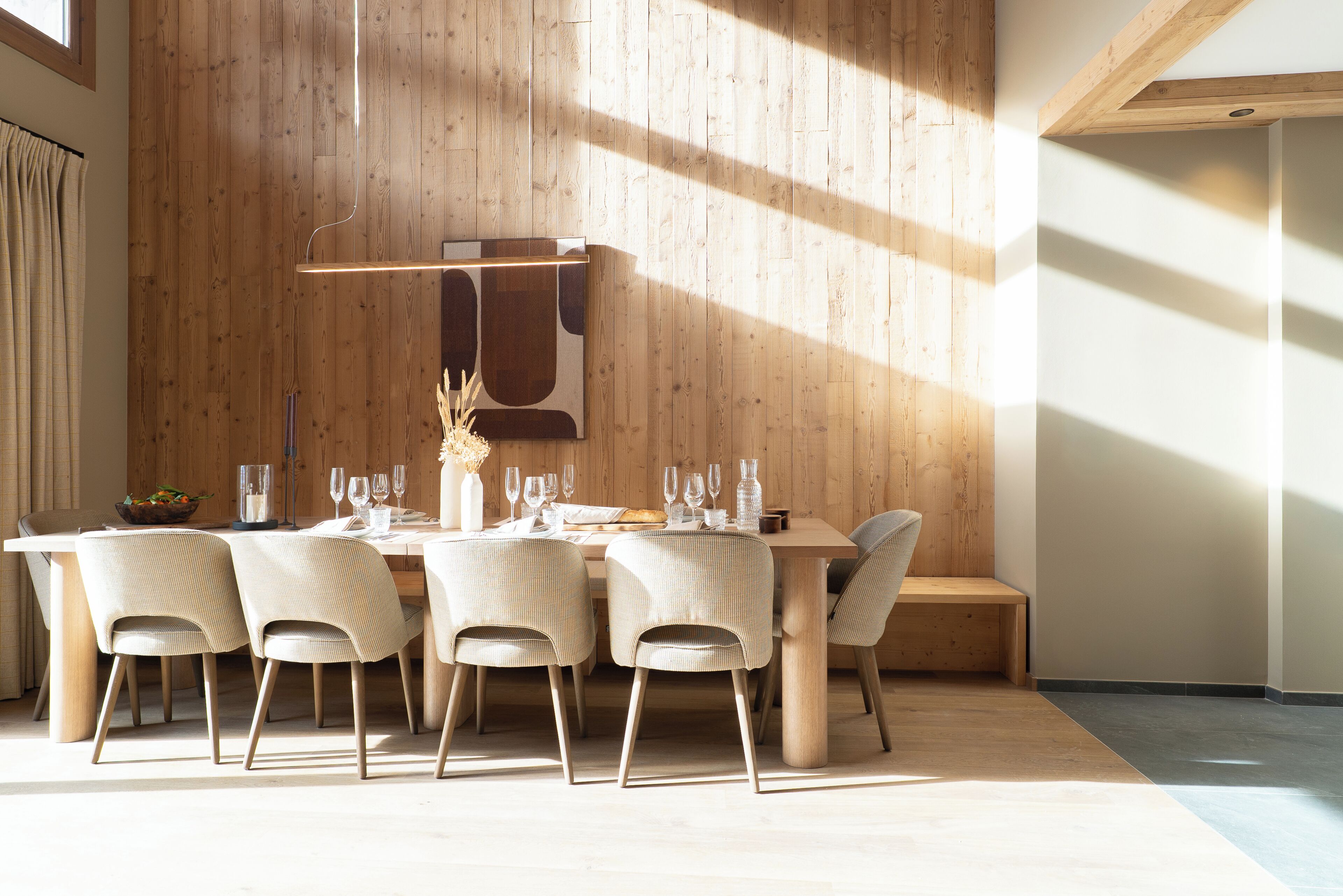Comedor con pared de madera, lámpara colgante y una mesa lista para cuatro comensales.