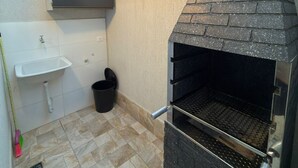 Uma cozinha externa compacta com churrasqueira, pia e lixeira.