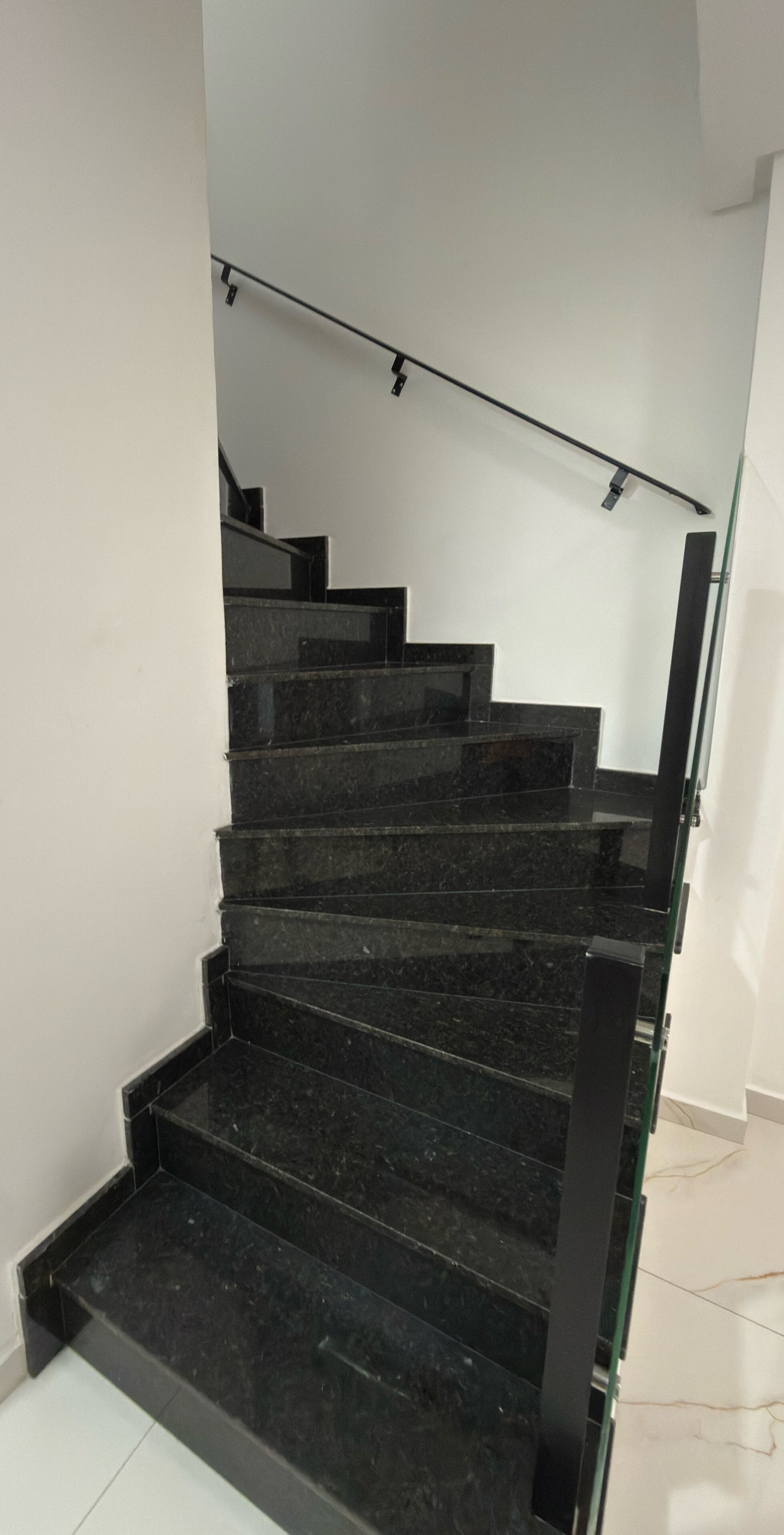 Un escalier avec des marches en marbre noir et une rampe en verre.