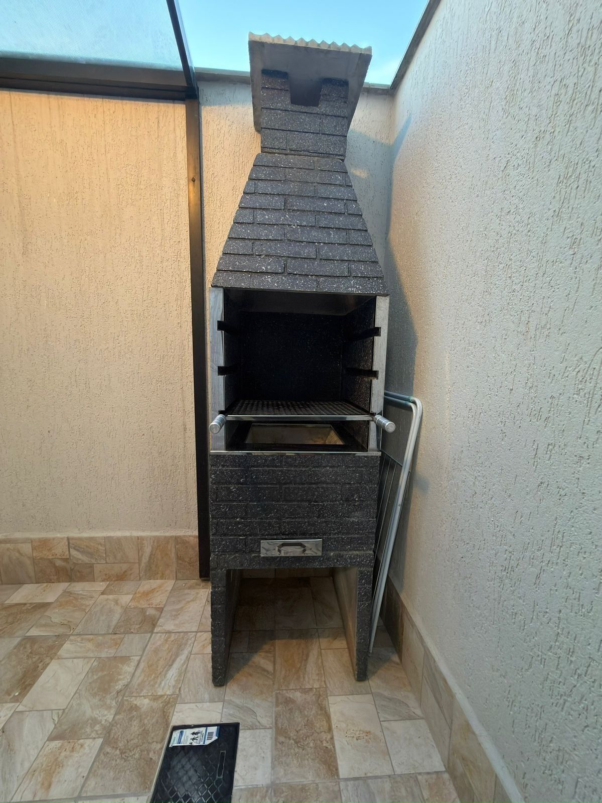 Ein gemauerter Grill für den Außenbereich mit Schornstein, einer Schiebetür und einem Metallrost.