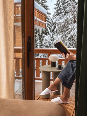 A person reading a book on a wooden deck with a view of snow-covered trees. - Hotel Barma Courchevel (Courchevel)