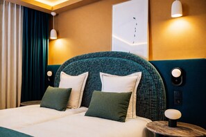 A hotel room with a large bed, two pillows, a headboard with a geometric pattern, wall-mounted lights, and a framed artwork above the bed. - Hotel Barma Courchevel (Courchevel)