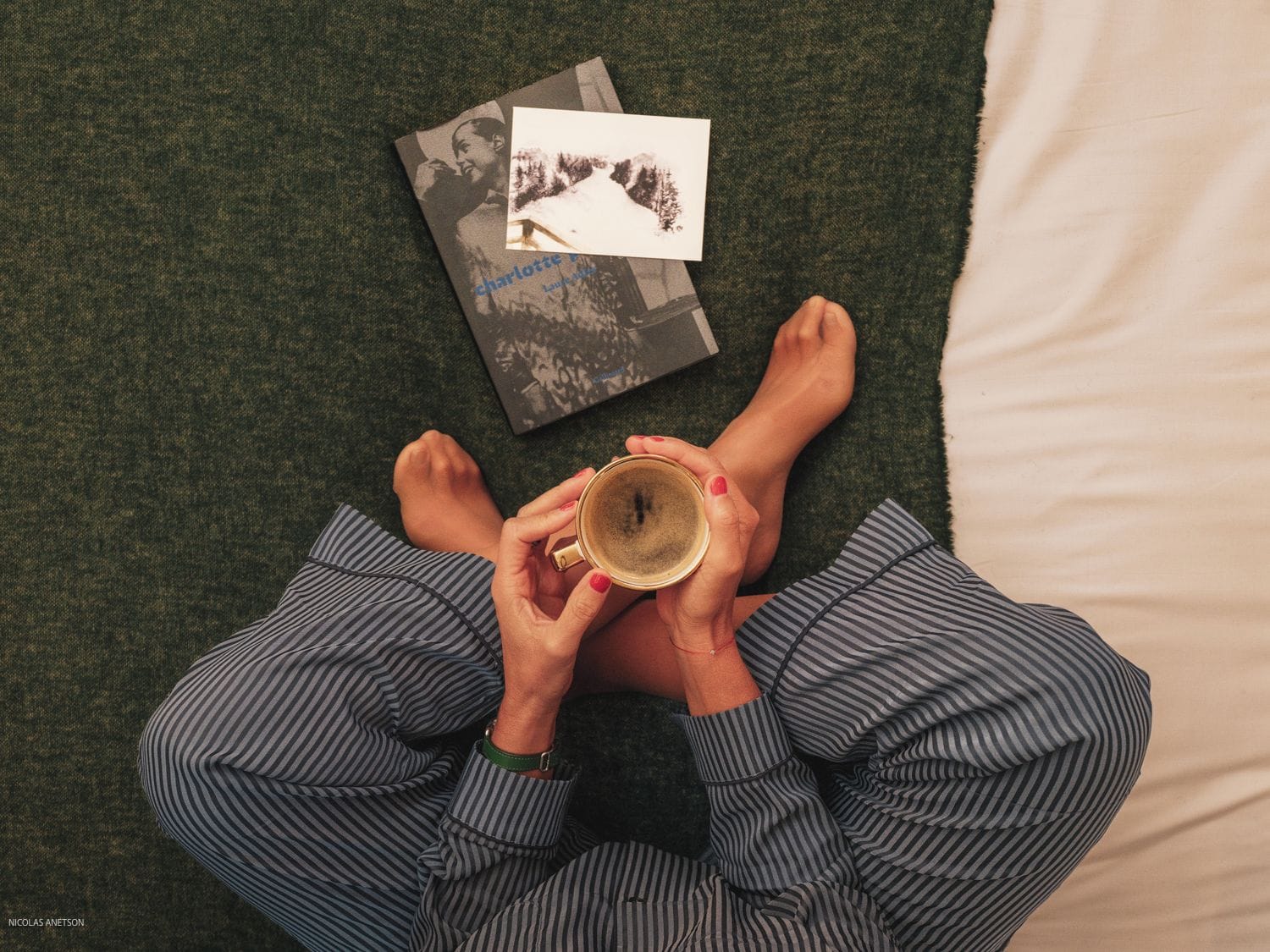 Una persona acostada en una cama con un libro y una taza.