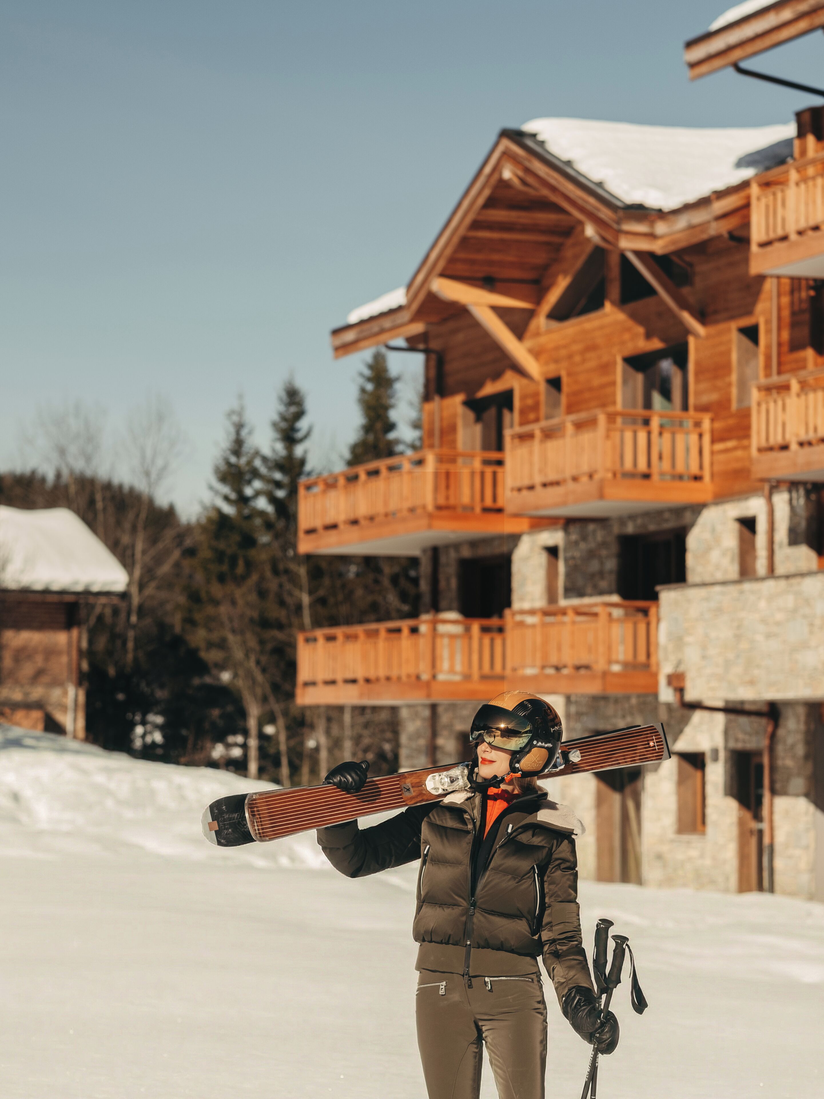A person with skis and ski poles, standing in a snowy area with a wooden building in the background.