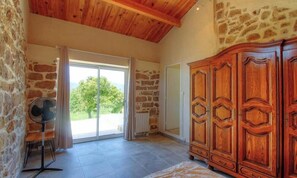 A room with stone walls, a wooden ceiling, a large wooden wardrobe, a fan, and a sliding glass door leading to a balcony. - U Caseddu - CUTTOLI CORTICCHIATO (CUTTOLI CORTICCHIATO)