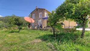 Ein Steinhaus mit rotem Dach, Sitzgelegenheiten draußen und einem Garten.