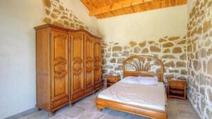 Ein Schlafzimmer mit einer Steinwand, einem Holzschrank und einem Bett mit einem hölzernen Kopfteil.