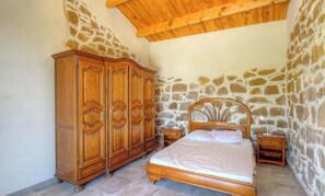 A bedroom with a stone wall, wooden wardrobe, and a bed with a wooden headboard. - U Caseddu - CUTTOLI CORTICCHIATO (CUTTOLI CORTICCHIATO)