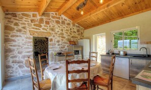 A rustic stone wall, wooden dining table, chairs, kitchen area with appliances, and a view through a window. - U Caseddu - CUTTOLI CORTICCHIATO (CUTTOLI CORTICCHIATO)