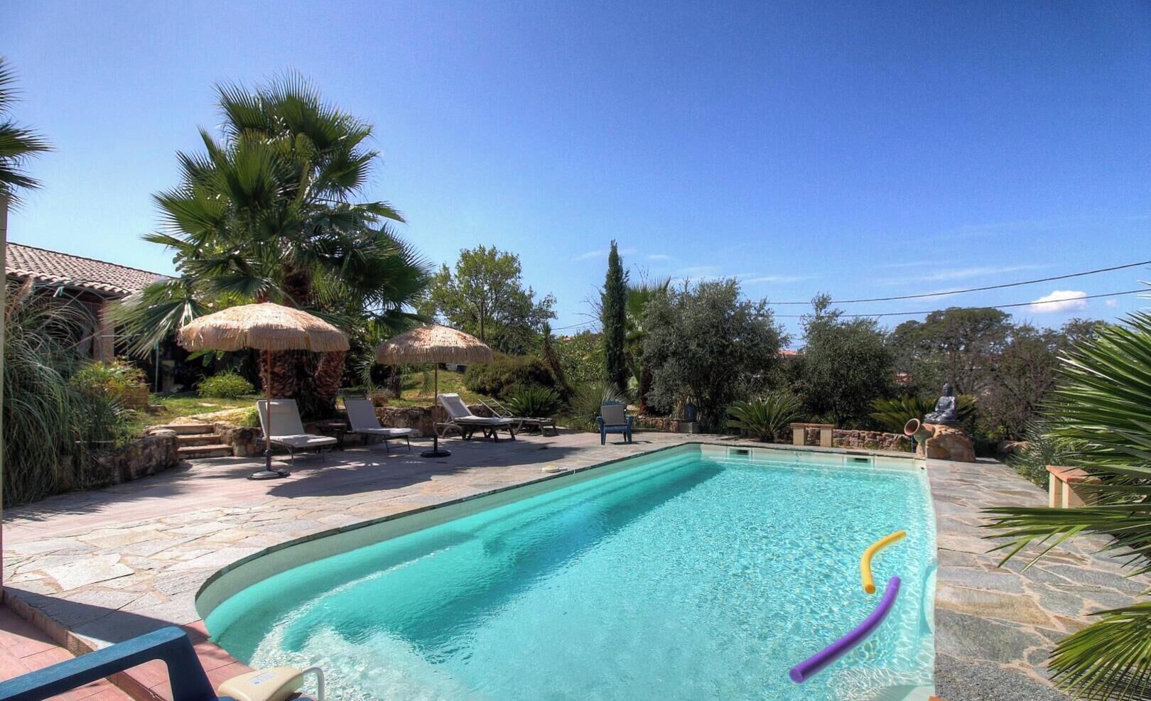 Une piscine entourée de verdure et agrémentée d’une statue, avec des chaises longues et des parasols à proximité.