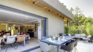 Ein offenes Wohnzimmer mit einem Essbereich, gedecktem Tisch, einer Küche im Hintergrund und einer Terrasse mit Sitzgelegenheit.