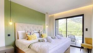Ein Hotelzimmer mit einem großen Bett, einem Balkon mit Sitzgelegenheiten und Blick ins Grüne.