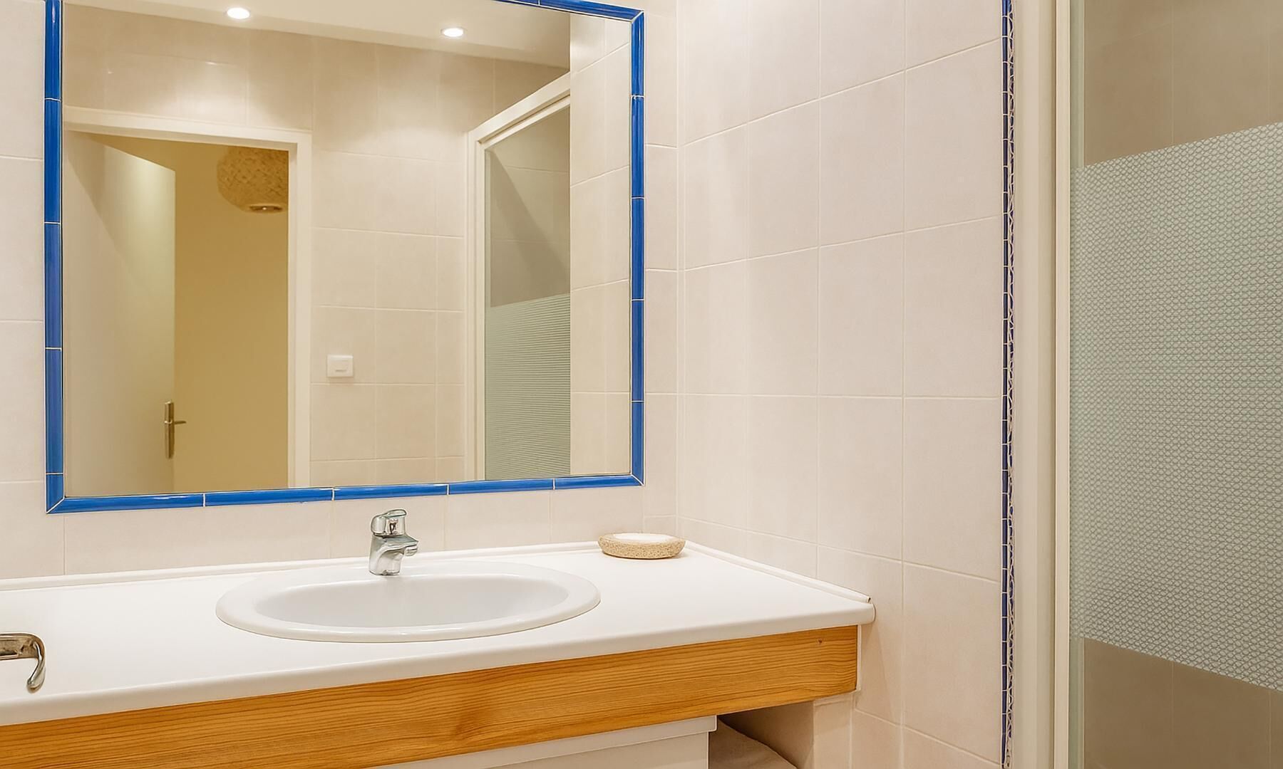 Un baño con un lavamanos blanco, un espejo con marco azul y zona de ducha.