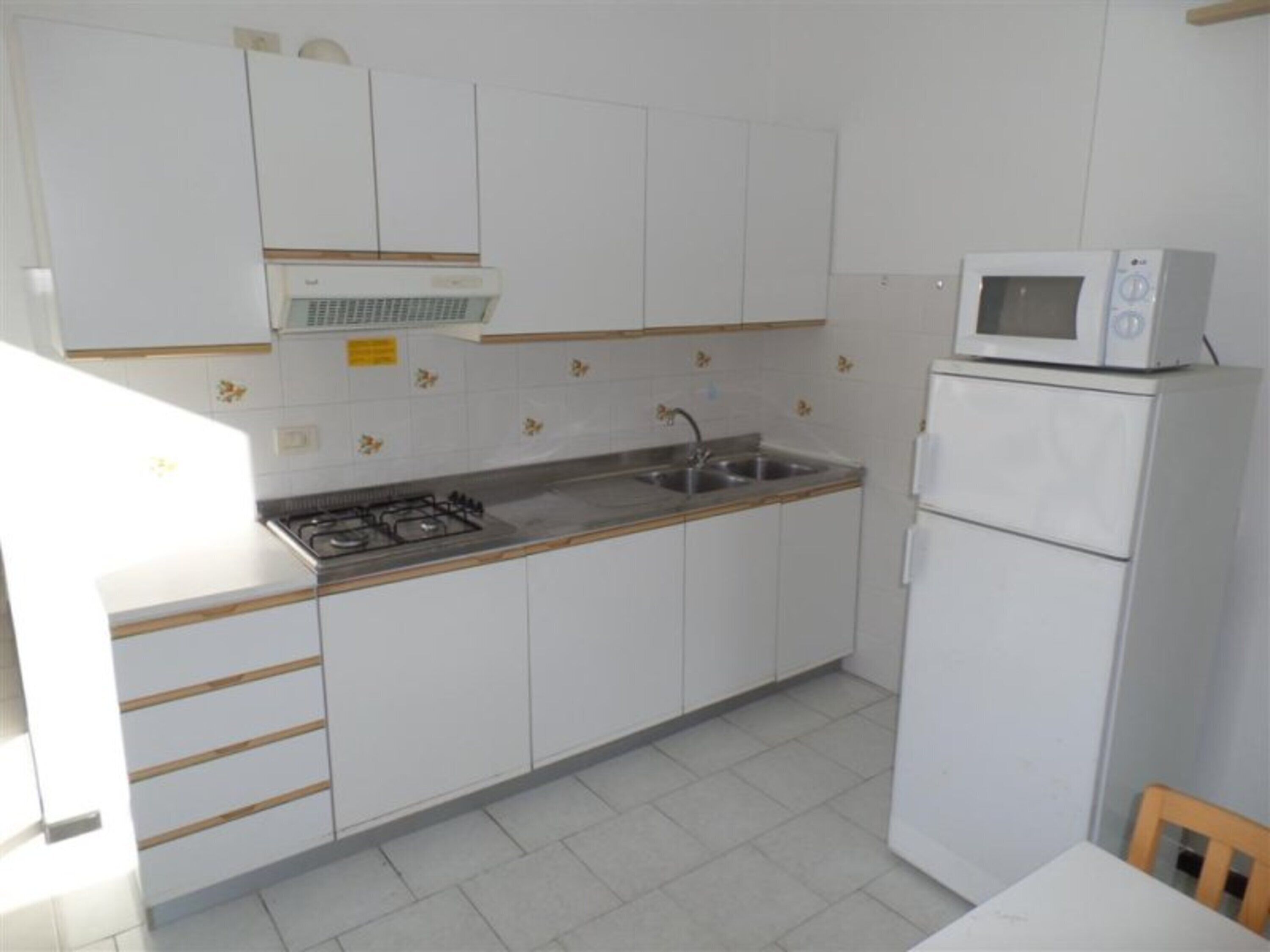 Une cuisine avec des meubles blancs, une cuisinière à gaz, un évier et un four à micro-ondes.