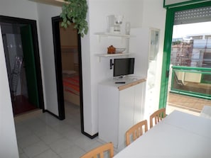 Eine kompakte Küche mit Mikrowelle, kleinem Kühlschrank und Fernseher. Es gibt einen Esstisch mit Stühlen und einen Blick nach draußen durch eine Glastür.
