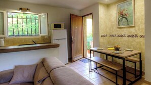 A compact kitchen with a microwave, refrigerator, and a dining area with a bench and table. - Rocca Rossa - PORTO VECCHIO (PORTO VECCHIO)