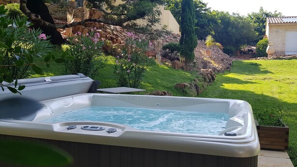A hot tub in a garden with a stone wall, a small building, and a grassy area. - Rocca Rossa - PORTO VECCHIO (PORTO VECCHIO)