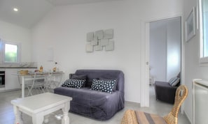 Ein modernes Wohnzimmer mit einem grauen Sofa, einem weißen Couchtisch und einem Essbereich mit einem kleinen Tisch und Stühlen.