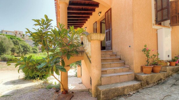 Un edifici amb una escala que mena a una porta, envoltat de plantes en testos i un camí de grava.