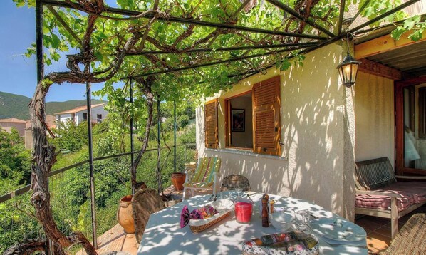 Ein sonniger Essbereich im Freien mit Tisch, Stühlen und einer Pergola mit Weinreben.