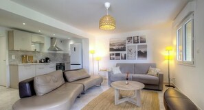 Ein modernes Wohnzimmer mit einer Couch, einem Couchtisch und einem Essbereich, wobei im Hintergrund eine Küche zu sehen ist.