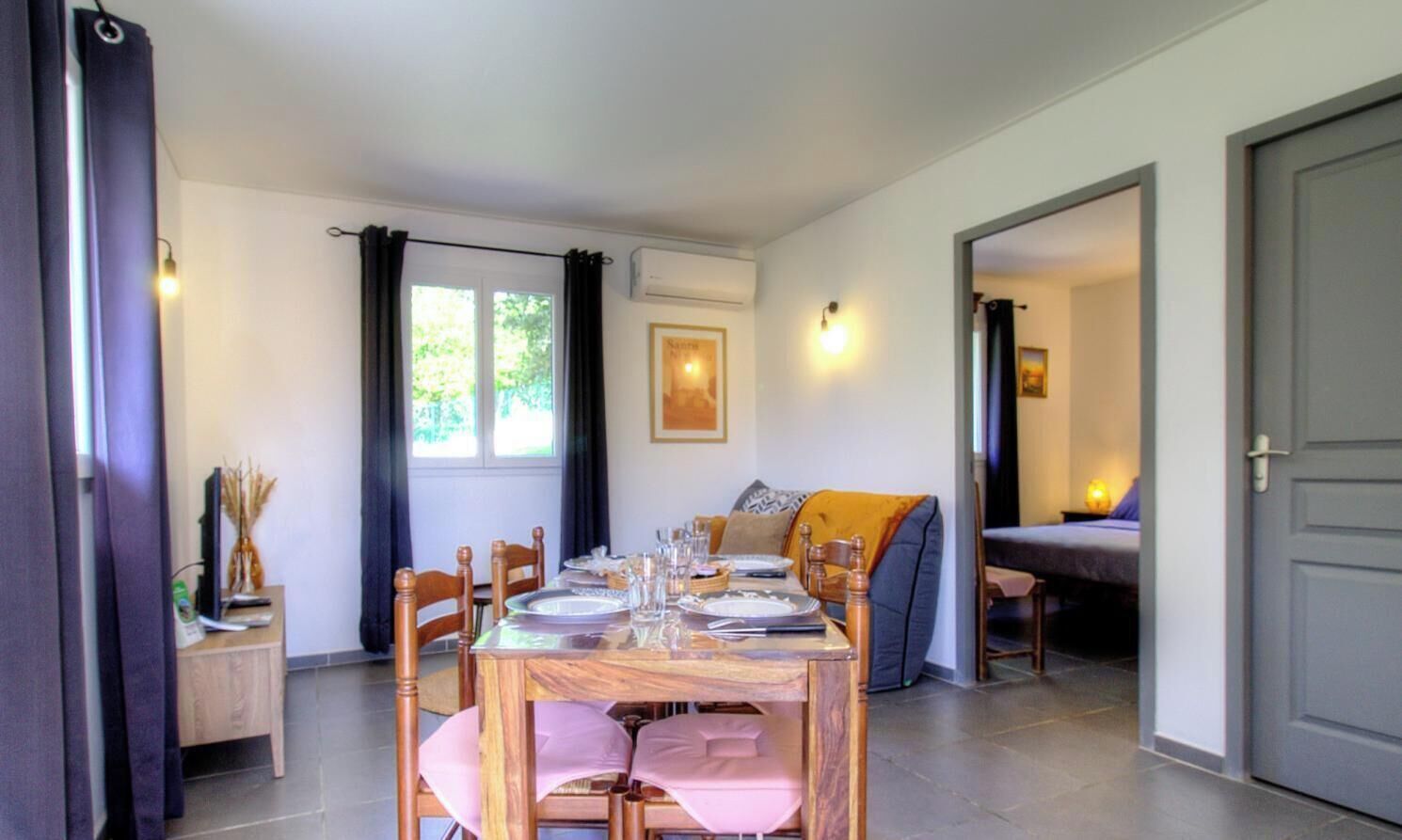 A dining area with a table set for four, a sofa, and a bed in the background.